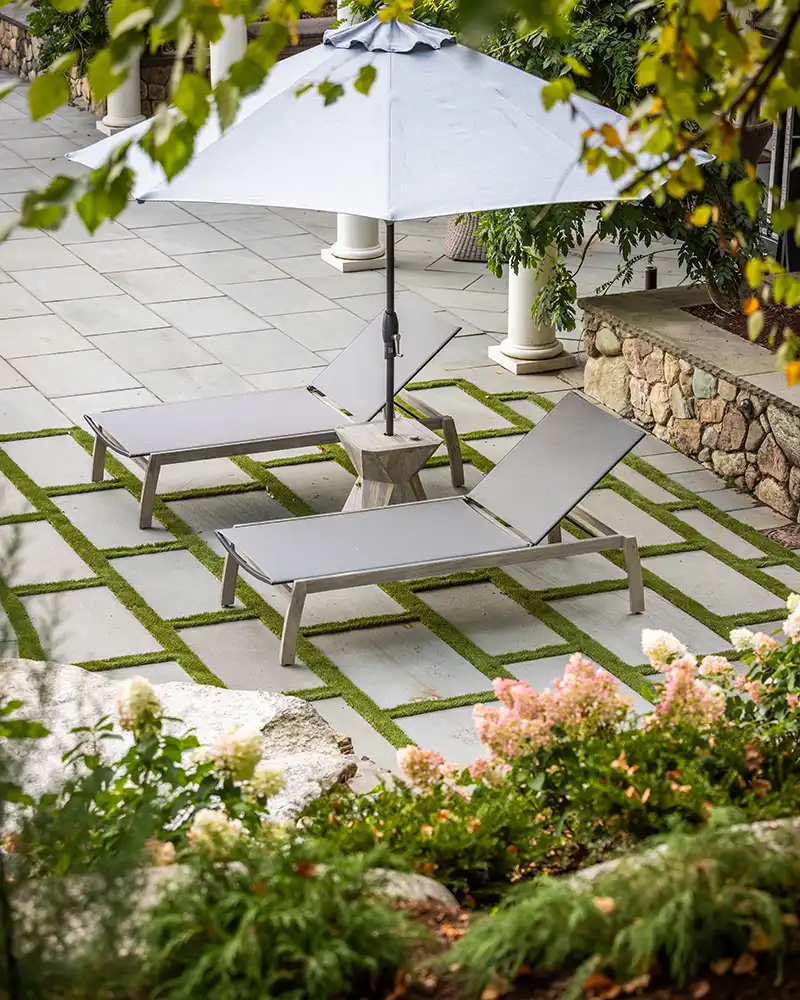 patio with grass surrounding pavers and lounge chairs